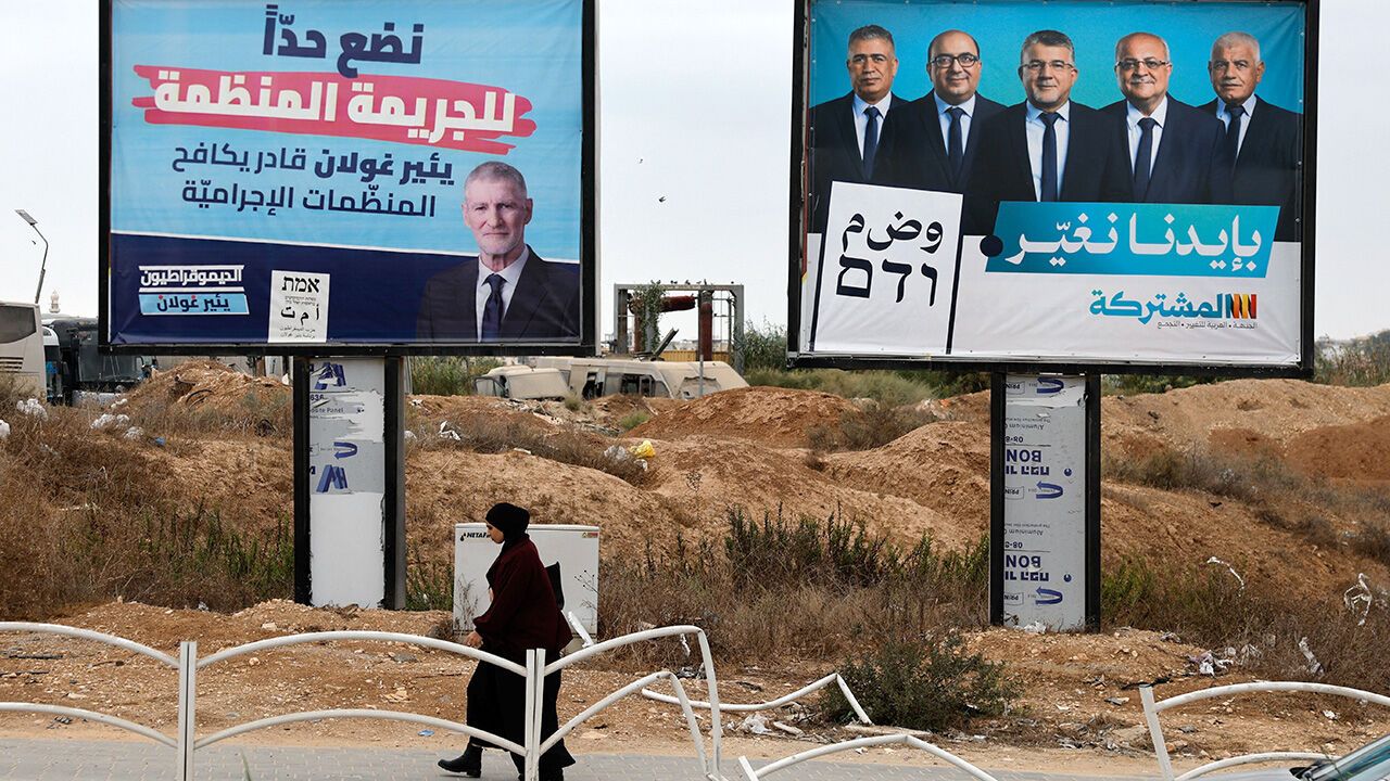 A woman walks past pre-election campaign billboards featuring Yair Golan of the Democrats party and leaders of the Joint List
