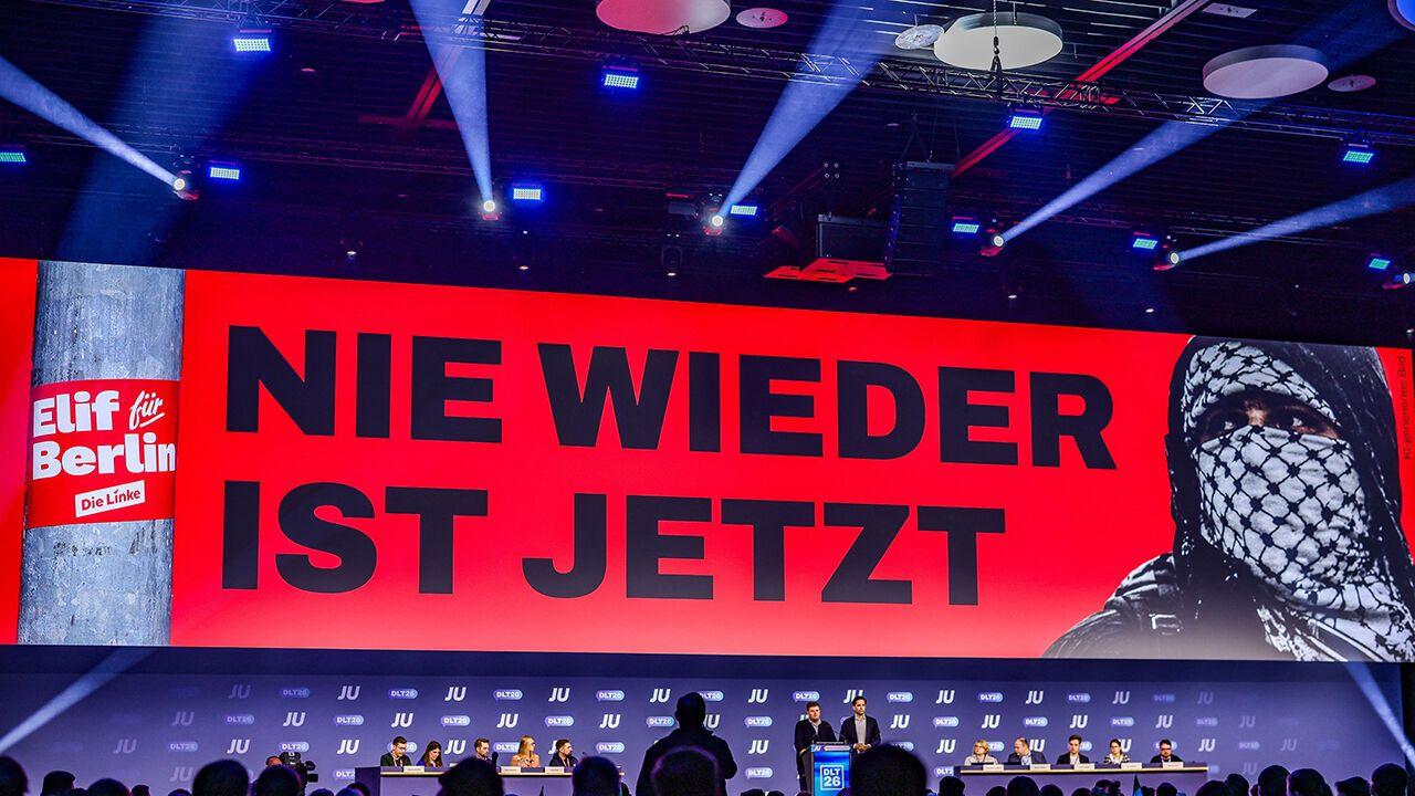 Members of Junge Union stand on stage with the slogan "Never is now" behind them