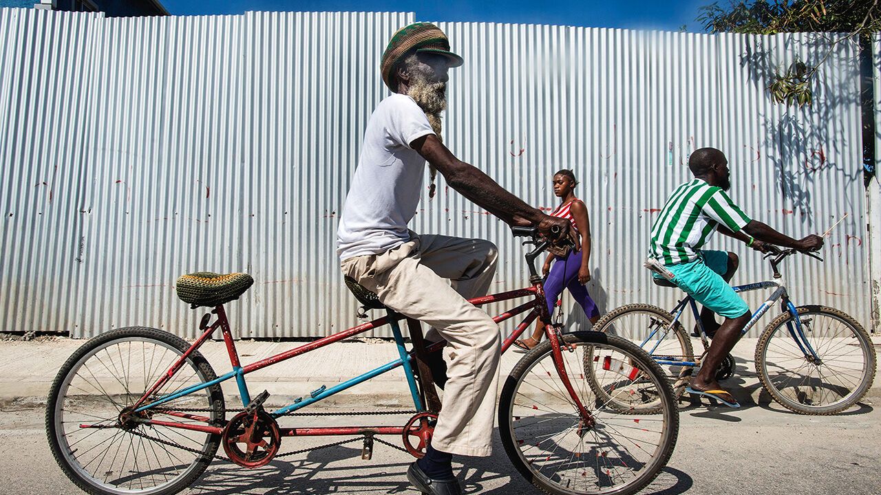 A Rastafarian man riding a tandem bicycle through the steets of Falmouth. Jamaica.